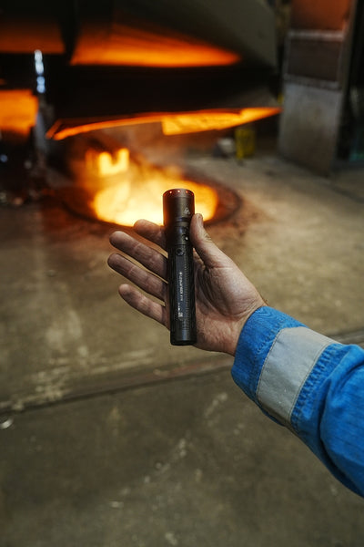 Ledlenser P7R Torch held in a worker’s hand in front of a glowing furnace compact rechargeable flashlight for professional use