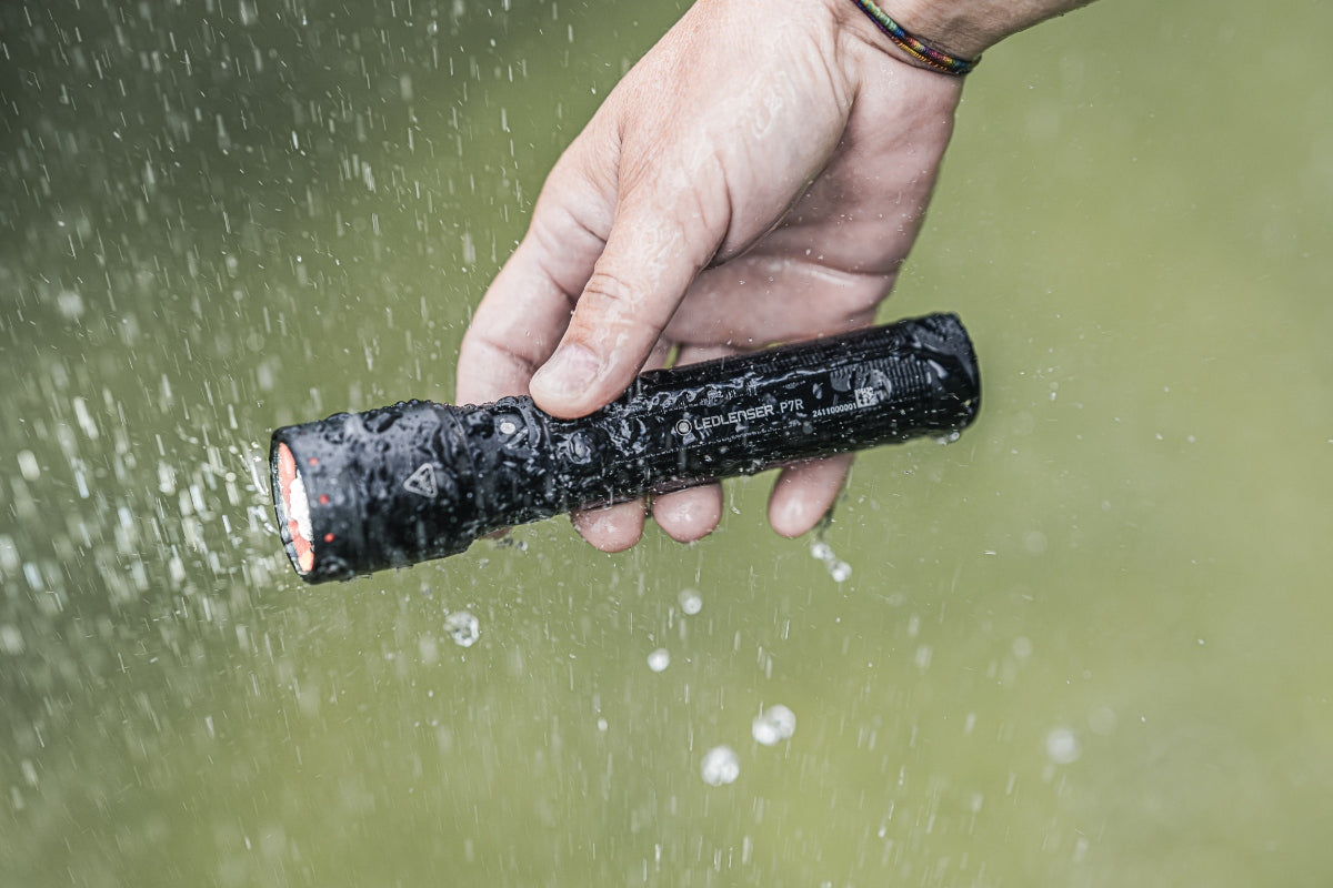 Ledlenser P7R Torch held in a rain soaked hand black compact rechargeable flashlight in use outdoors