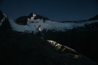 Ledlenser P7R Torch in use on a rocky mountain ledge at night person holding a compact rechargeable flashlight emitting a bright beam