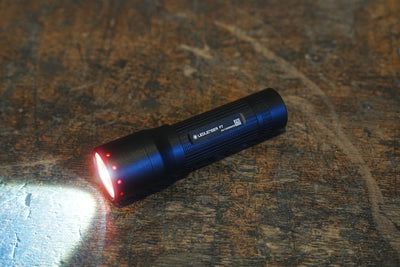 Ledlenser P7 Torch on a wooden surface angled to show its LED front with red indicators and beam