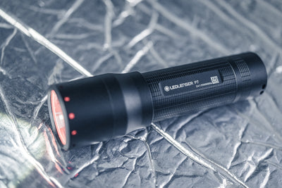 Ledlenser P7 Torch compact black flashlight with red indicator dots on the head lying on a crumpled surface
