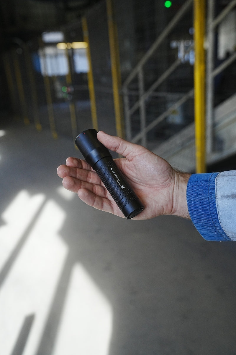 Ledlenser P7 Torch held in a hand compact black flashlight with textured grip in an indoor industrial setting