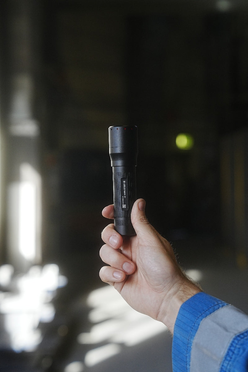 Ledlenser P7 Torch held in a hand compact black flashlight with red indicator lights against a dark background