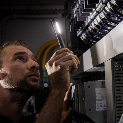 Ledlenser W2R Work Pen and Test Light held by a technician inspecting equipment rack in a server room