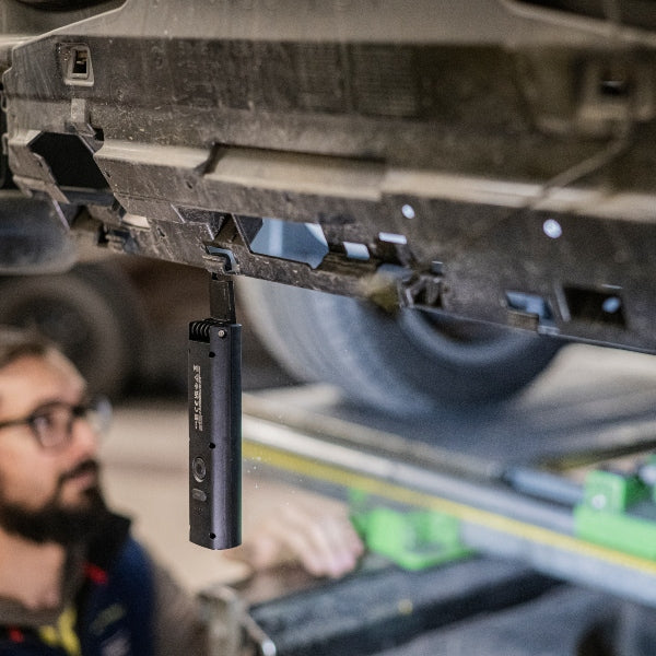Ledlenser W5R Work Light hanging from a vehicle undercarriage in a workshop with a technician in the background