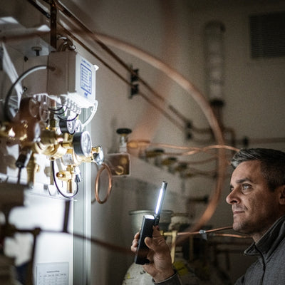 W6R Work Light held by a technician in an industrial control room illuminating valve panels and copper piping
