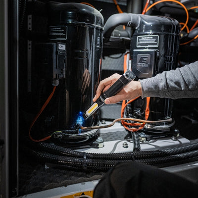 Ledlenser W7R Work Light being used handheld near industrial battery pods with orange cables; user in a gray sleeve operating the light