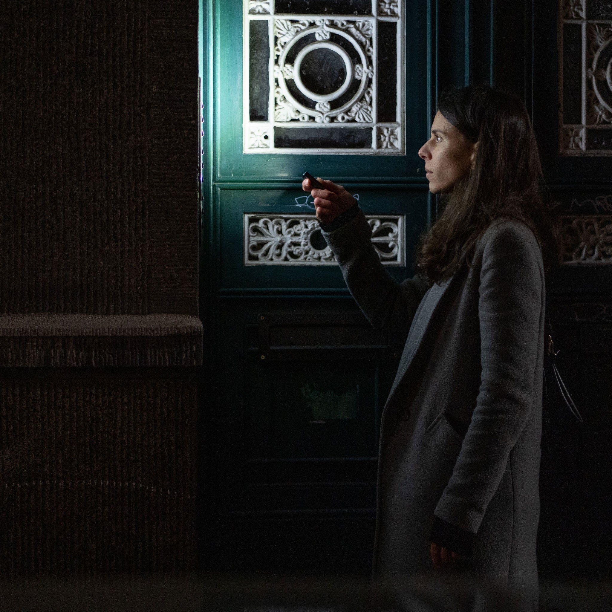 K4R Keychain Light held by a woman in a grey coat at night beside a decorative door; compact black keychain flashlight