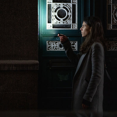 K4R Keychain Light held by a woman in a grey coat at night beside a decorative door; compact black keychain flashlight