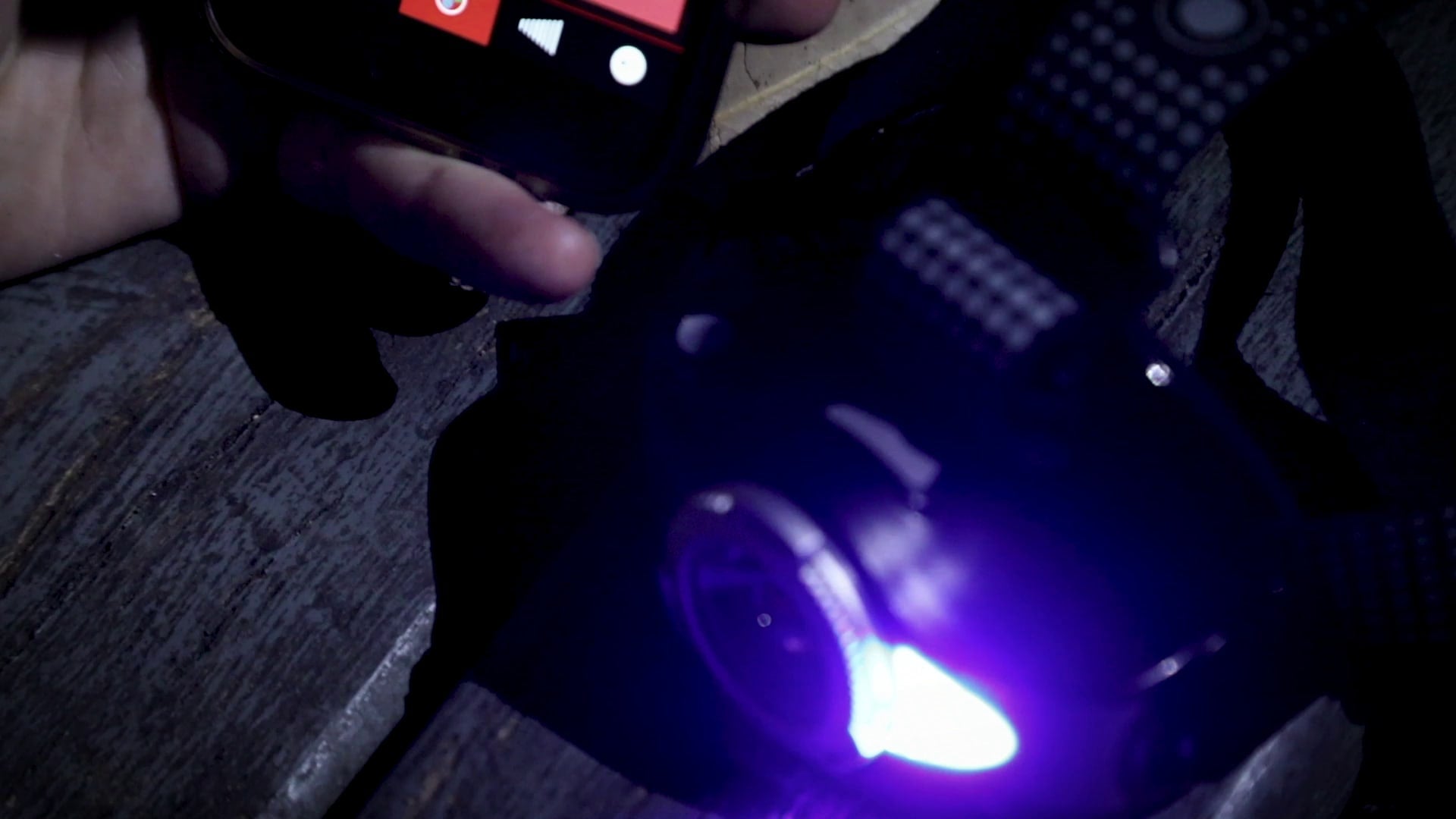 MH11 Blue Outdoor Headlamp powered on emitting blue light held by hand with the headlamp strap visible on a dark wooden surface