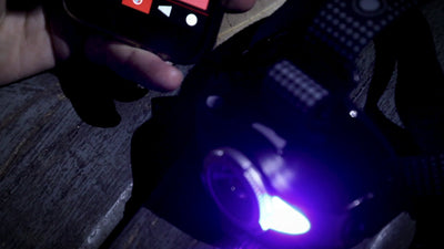 MH11 Blue Outdoor Headlamp powered on emitting blue light held by hand with the headlamp strap visible on a dark wooden surface
