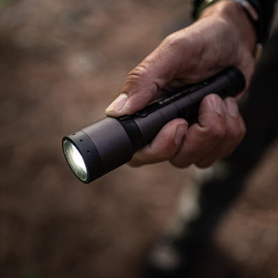 P7R Signature Torch held in a hand angled view showing its dark metallic body with the front LED illuminated