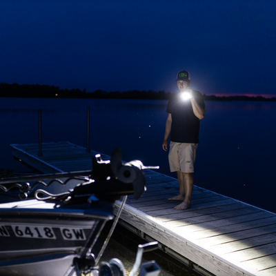 Ledlenser P18R Signature Torch held by a man on a wooden dock at night beam lighting a lakeside scene with a boat nearby