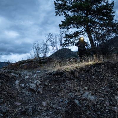 Ledlenser MH4 Powercase Combo headlamp and charging case in use on a hiker standing on rocky terrain at dusk with headlamp illuminated