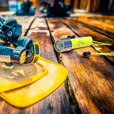 D14 2 Battery Operated Torch yellow green compact flashlight with silver bezel on a wooden workbench beside a yellow safety helmet