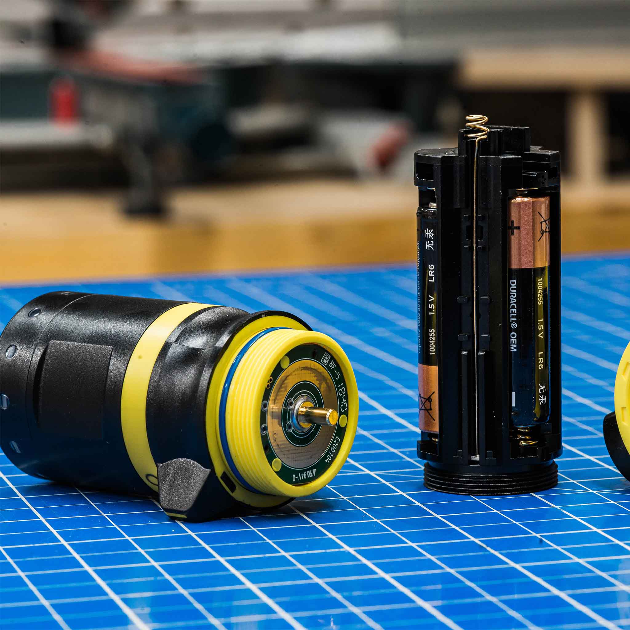 EX7 Torch disassembled components on a blue grid workbench showing the yellow accented body and battery cartridge layout