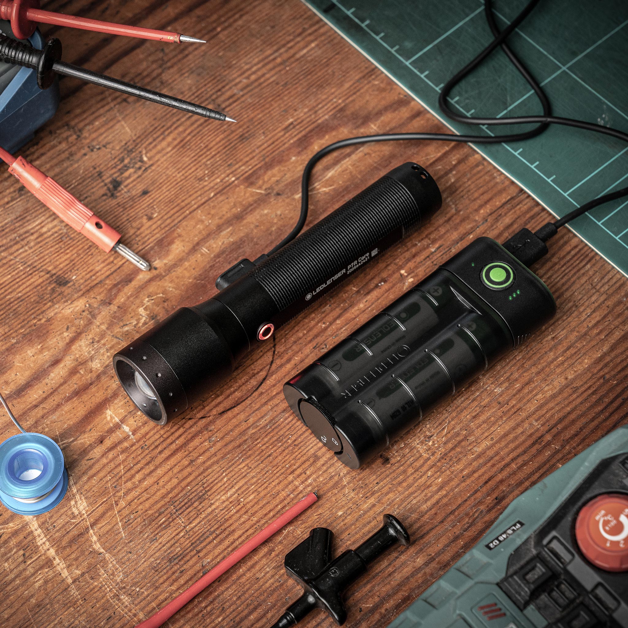 Ledlenser Flex7 Powerbank and a black flashlight on a wooden workbench with tools and a green cutting mat in the background