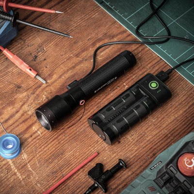 Ledlenser Flex7 Powerbank and a black flashlight on a wooden workbench with tools and a green cutting mat in the background