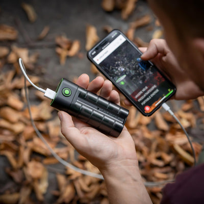 Ledlenser Flex7 Powerbank held in hand outdoors charging a smartphone via USB C with a compact black cylindrical design and green ring detailing