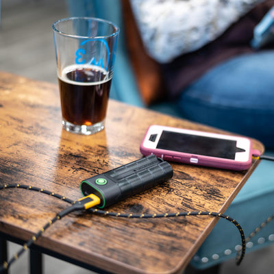 Ledlenser Flex7 Powerbank connected by a charging cable to a pink smartphone on a wooden table beside a glass of dark beer