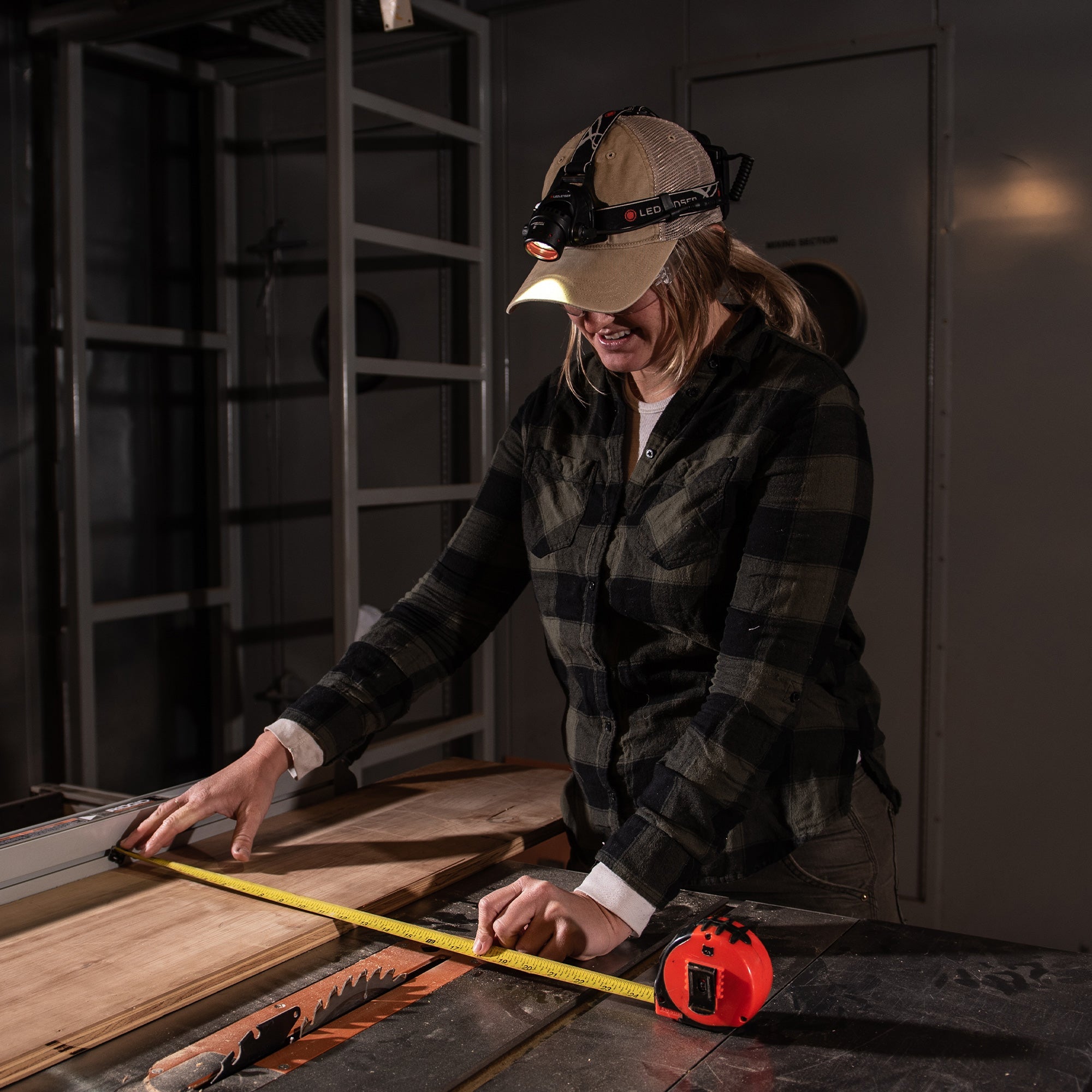 Ledlenser H14R 2 Headlamp worn by a woman in a plaid shirt using a measuring tape on a workshop table