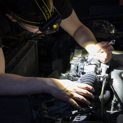 H15R Work Headlamp worn by a mechanic inspecting a car engine with the headlamp emitting light on the engine