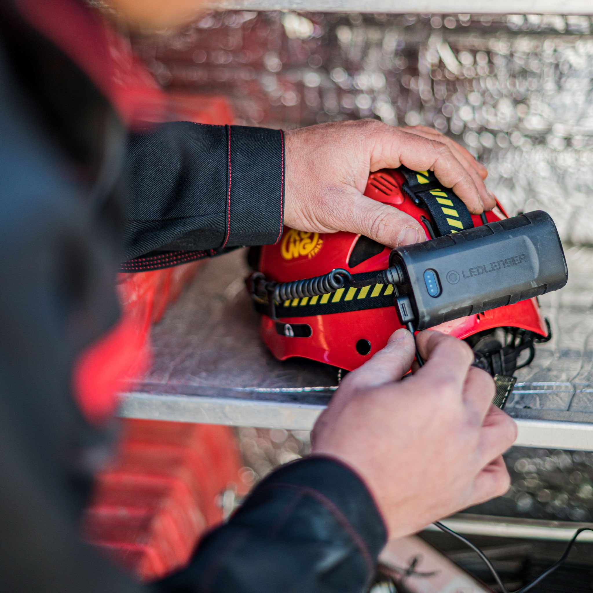 Ledlenser H15R Work Headlamp attached to a red safety helmet with a black and yellow strap on a metal work surface