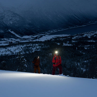 H19R Signature Headlamp worn by a hiker in a snowy mountain night scene with a bright beam; another climber in an orange jacket nearby
