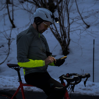 Ledlenser H19R Signature Headlamp mounted on a helmet worn by a cyclist in a snowy outdoor scene examining a handheld device