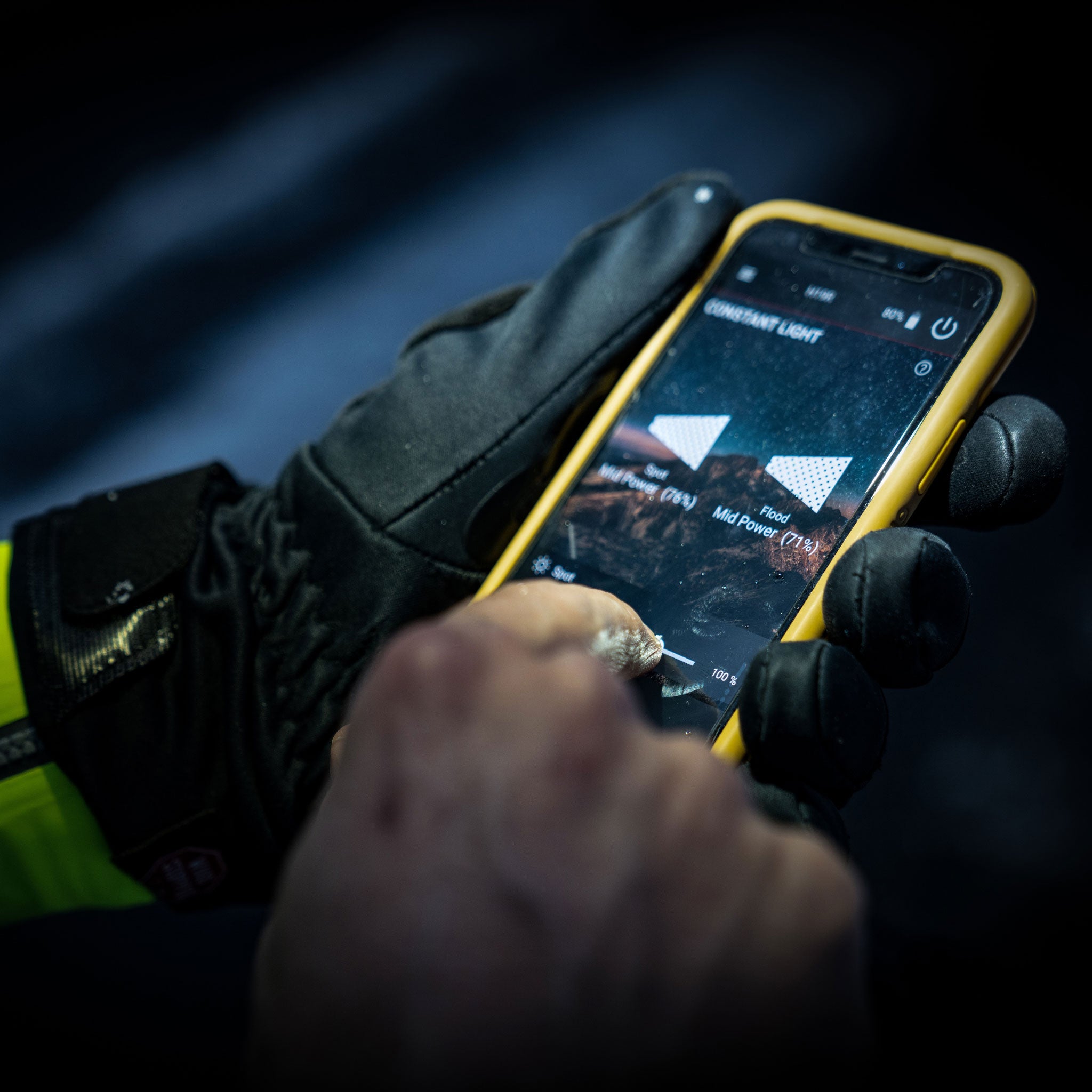 Ledlenser H19R Signature Headlamp being configured on a smartphone held by a gloved hand with a yellow phone case in a dark background