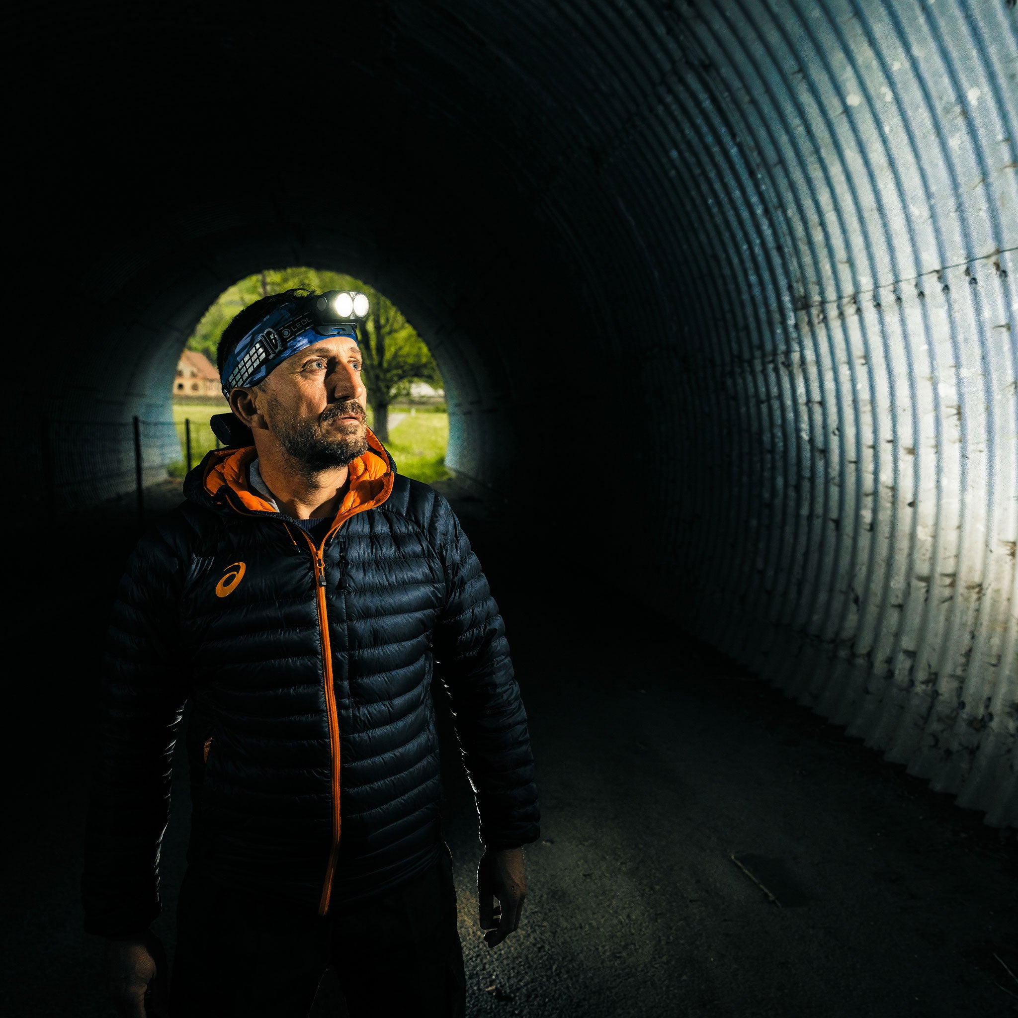 Ledlenser H19R Signature Headlamp worn on a man's head inside a dim tunnel; two bright LEDs visible on the headlamp