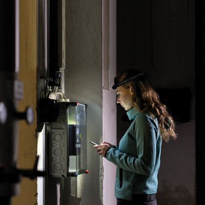 Ledlenser H4 Headlamp worn by a woman in a dim utility room inspecting an electrical panel with a focused beam