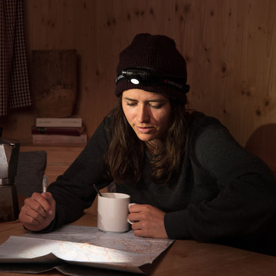 Ledlenser H5 Core Headlamp worn on a black headband positioned on the forehead indoors with a map and mug on a wooden table