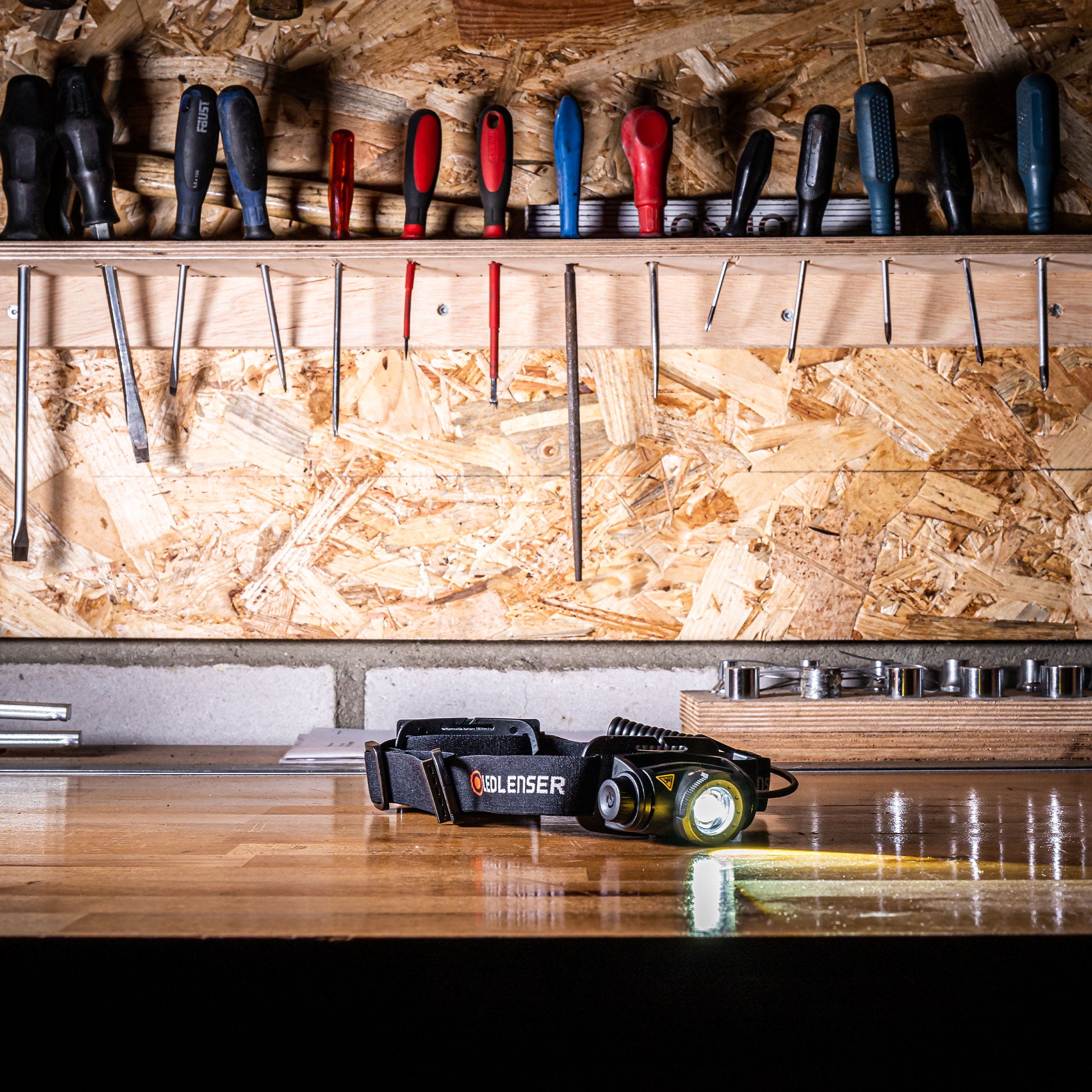 Ledlenser H5R Core Headlamp lying on a wooden workshop bench with a black strap and a tool shelf in the background