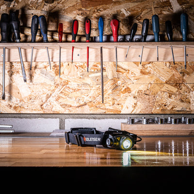 Ledlenser H5R Core Headlamp lying on a wooden workshop bench with a black strap and a tool shelf in the background