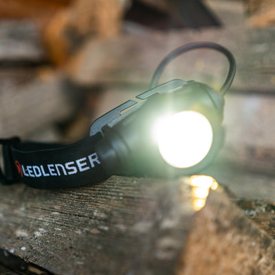 Ledlenser H7R Core headlamp with black adjustable strap showing the illuminated front light on a wooden surface