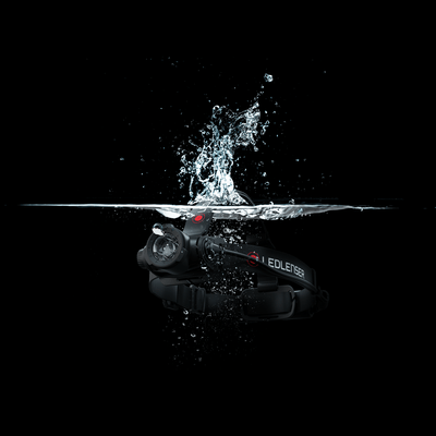 Ledlenser H7R Core Headlamp submerged in water with splashes black headlamp on an adjustable headband with red power button visible