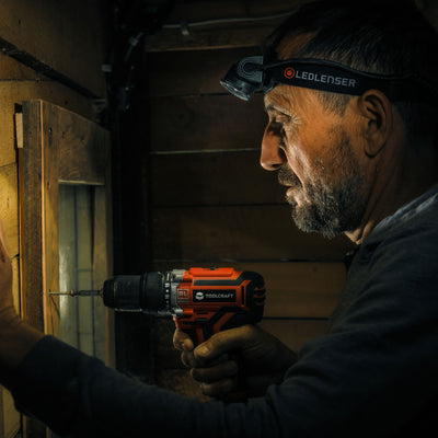 Ledlenser H7R Core Headlamp worn by man while drilling into a wooden board in a dim workshop