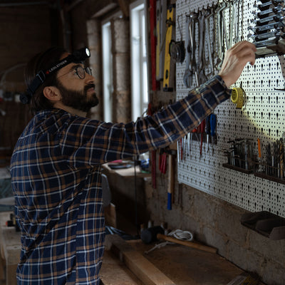 Ledlenser H7R Core Headlamp worn by man in a workshop adjusting tools on a pegboard workbench