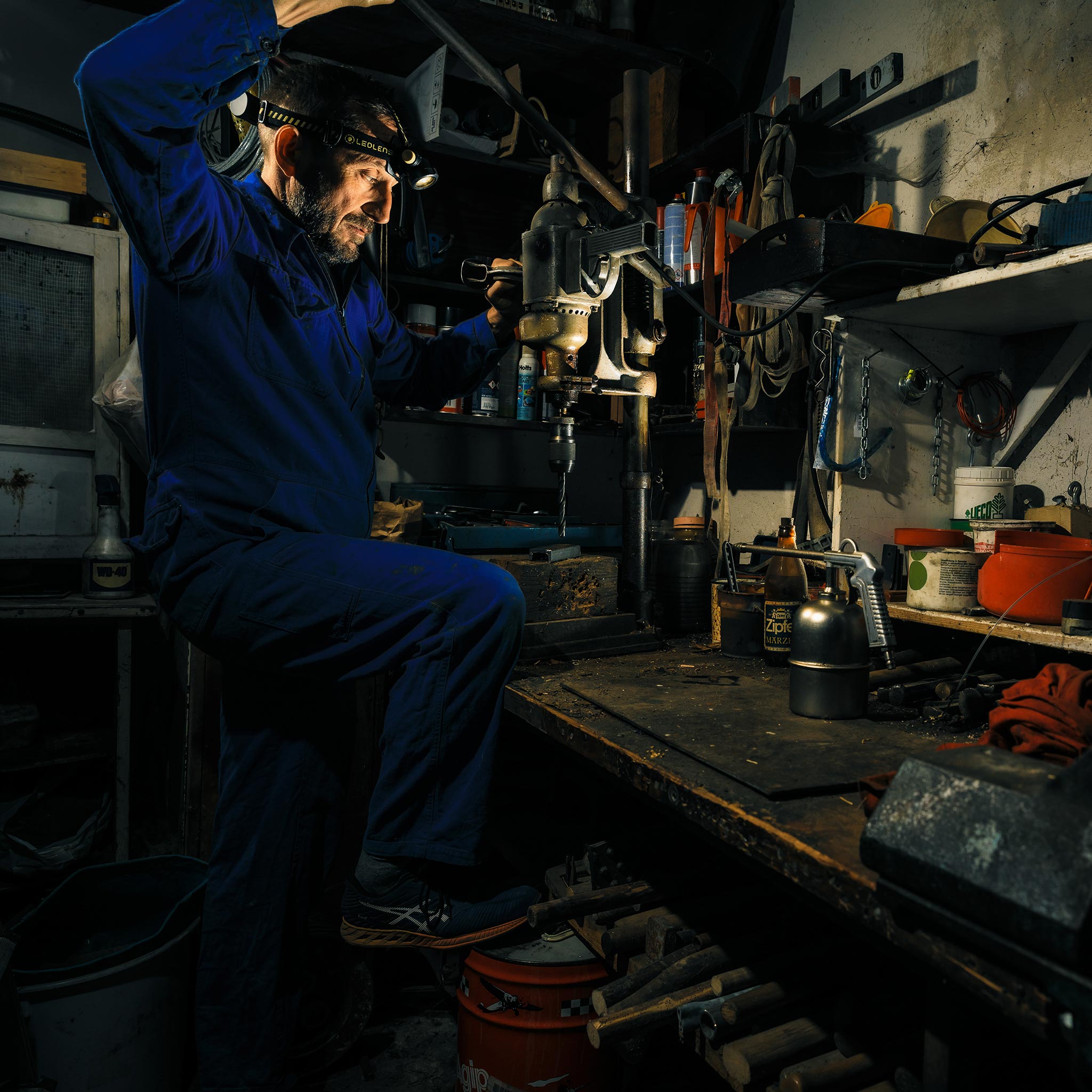Ledlenser H7R Work Headlamp worn by a craftsman in a cluttered workshop operating a drill press