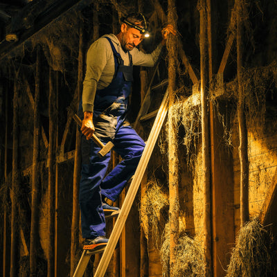 Ledlenser H7R Work Headlamp worn on the head by a man on a ladder in a dim workshop with a hammer showcasing professional work lighting