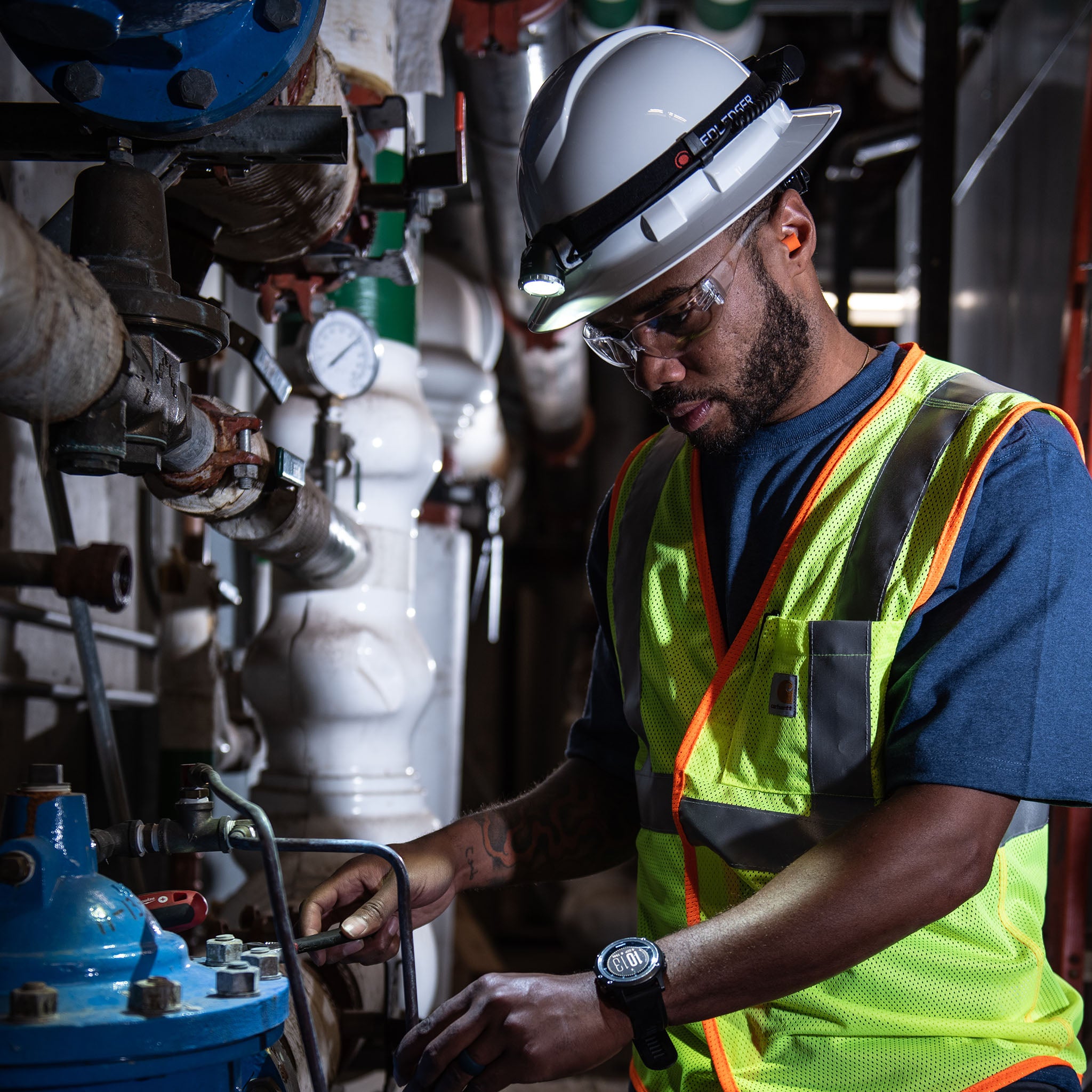 H8R Headlamp worn by a worker with a safety helmet and high vis vest inspecting industrial pipes with the light