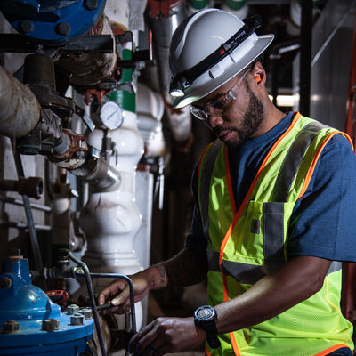 H8R Headlamp worn by a worker with a safety helmet and high vis vest inspecting industrial pipes with the light