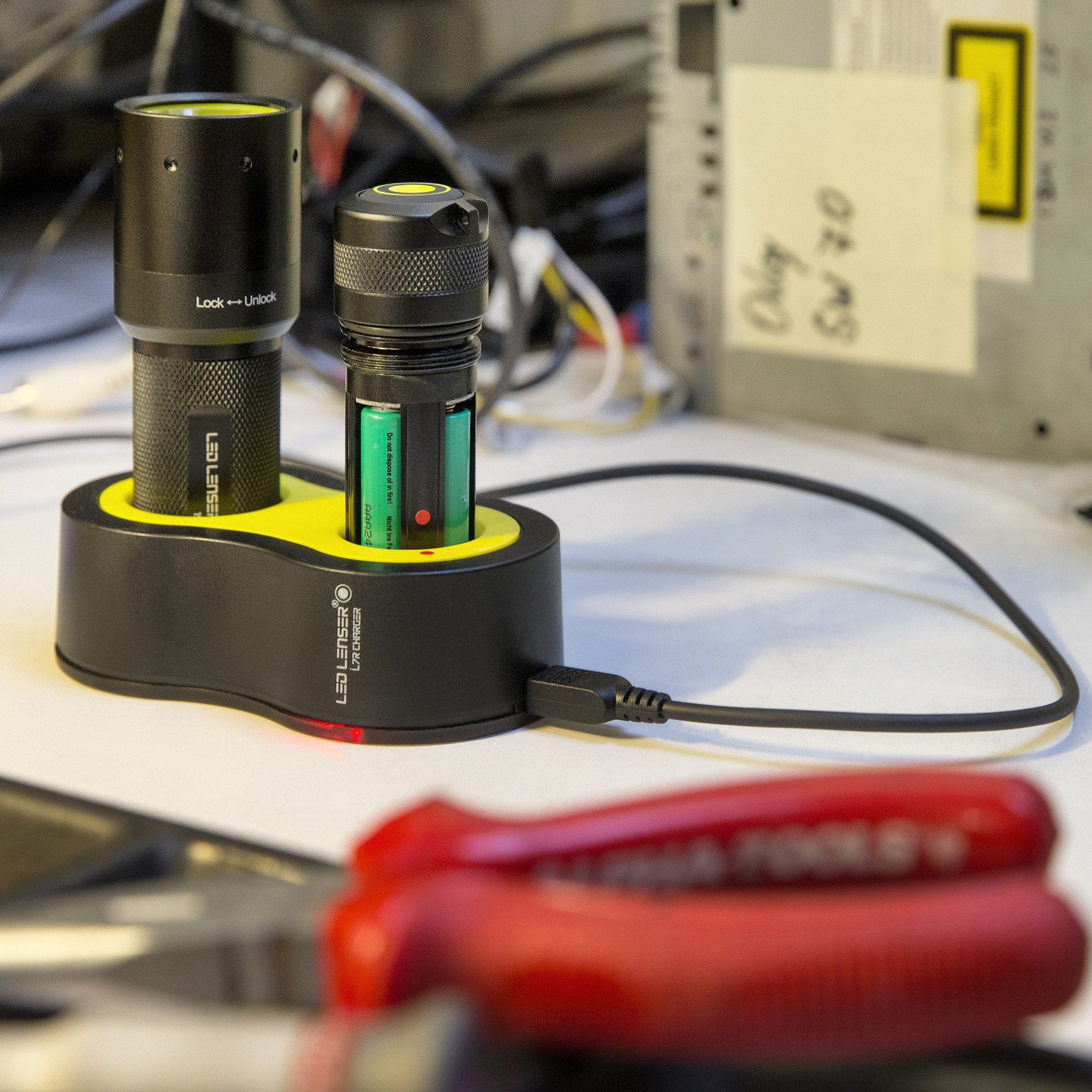 i7R Rechargeable Torch in a dual bay charging dock with yellow interior USB power cable attached on a workbench