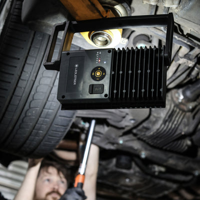 iF8R Spotlight by Ledlenser mounted under a car during repair showing a black rugged work light with control dial and cooling fins