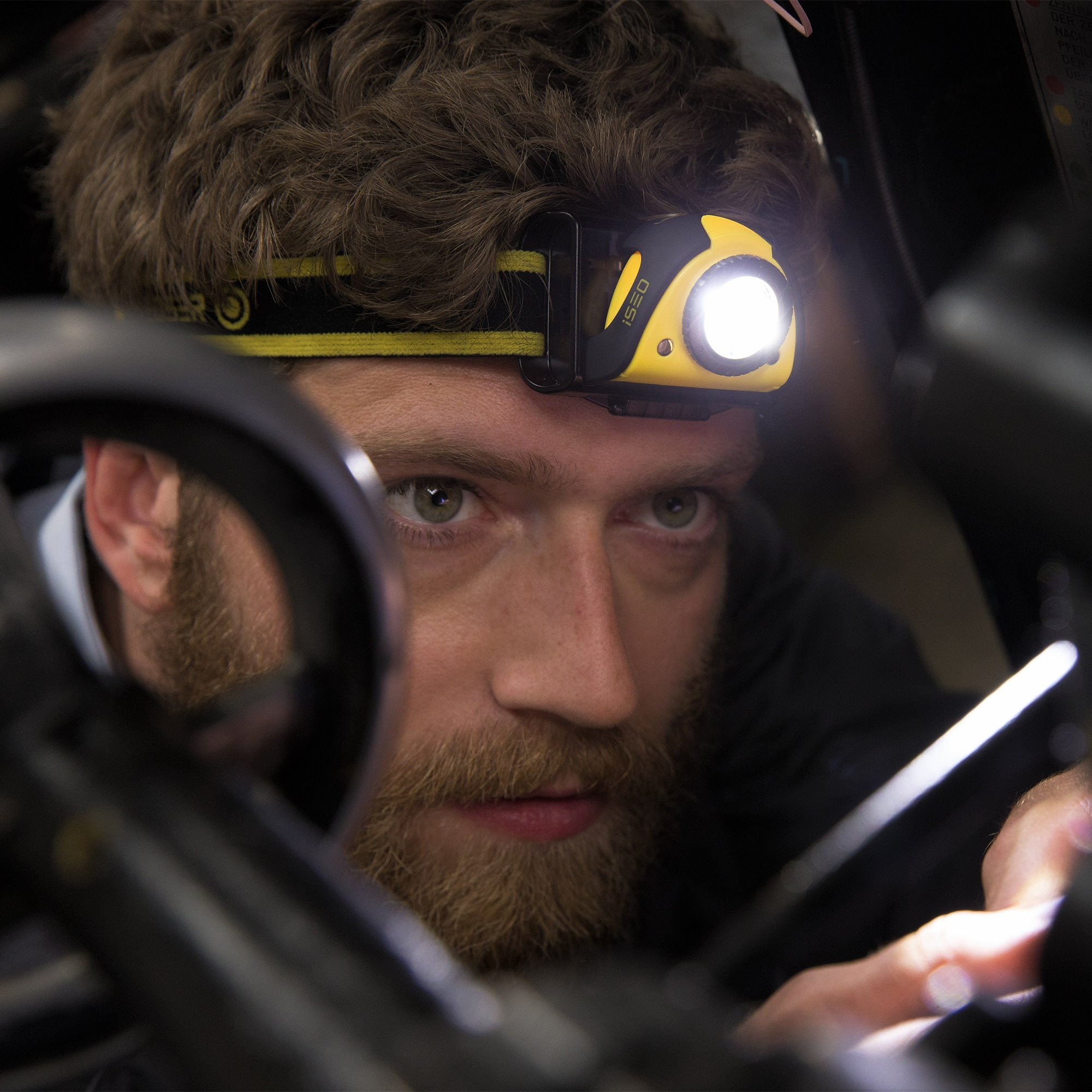 iSEO5R Rechargeable Headlamp worn on a yellow and black headband with the light on close up of a person using it