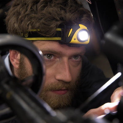 iSEO5R Rechargeable Headlamp worn on a yellow and black headband with the light on close up of a person using it