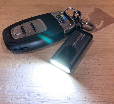 K4R Rechargeable Key Ring Lamp compact black key ring flashlight shown with light on and key chain on a wooden surface