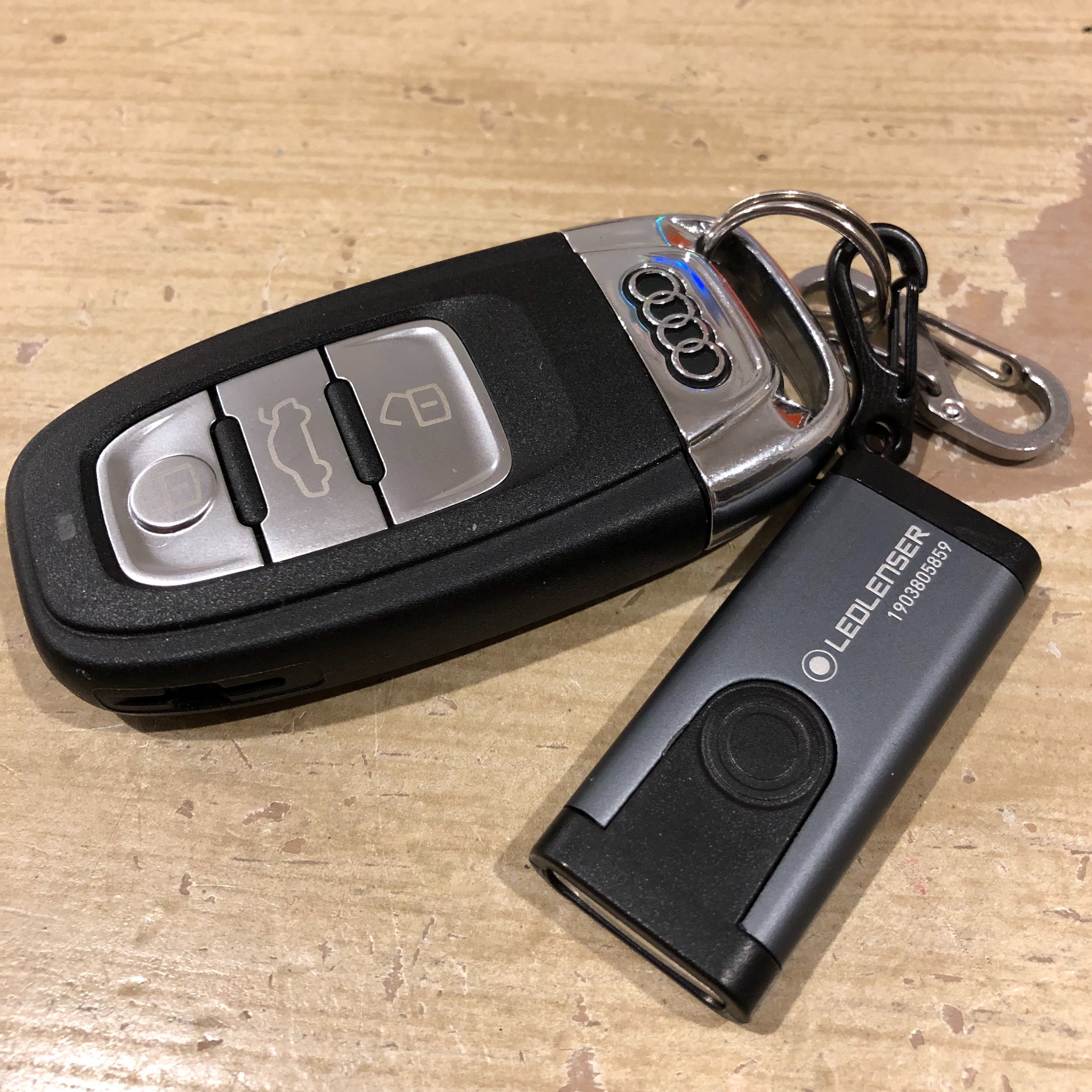 Ledlenser K4R rechargeable key ring lamp on a keychain with black and grey housing shown on a wooden surface with lid and ring accessories visible