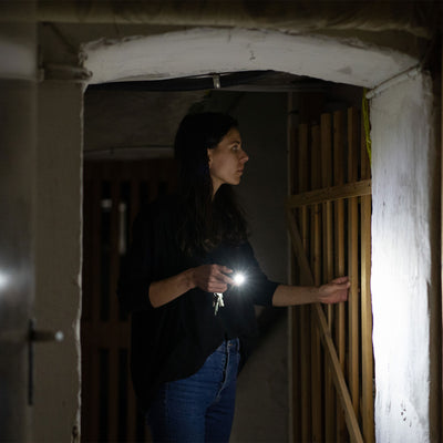 Ledlenser K6R Keychain Light held by a woman in a dark unfinished interior beam shining from a compact black keyring flashlight